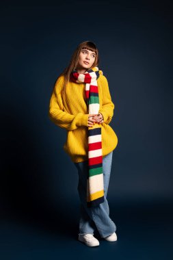 Genç bir kadın rahat bir süveter ve renkli bir eşarpla poz veriyor, sonbaharın sıcaklığını kucaklıyor..