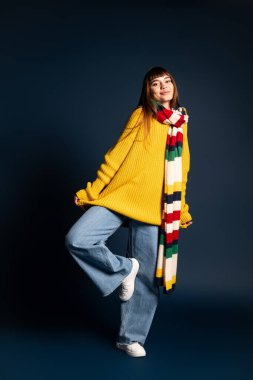Genç bir kadın rengarenk sonbahar kıyafetleri içinde neşe içinde poz verirken sıcaklık ve tarz saçar..