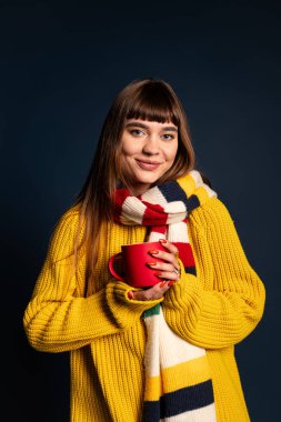 Canlı bir süveter giyen neşeli genç bir kadın elinde kırmızı bir bardak tutuyor, sıcaklık ve tarz saçıyor..