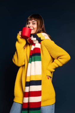 Aydınlık elbiseli kendine güvenen genç bir kadın koyu bir arka planda kırmızı bir kupa tutuyor..