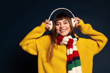 Sarı kazaklı neşeli genç bir kadın müzik dinlerken gülümsüyor..