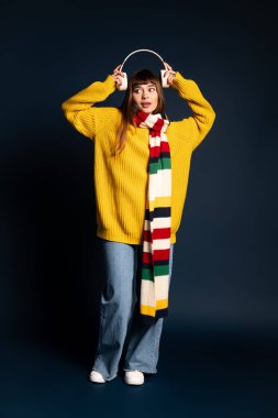 Enerjik genç kadın kulaklıklarla poz veriyor, şık, sıcak elbisesini ve canlı atkısını sergiliyor..