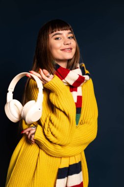 Güzel genç bayan, rahat bir elbise içinde, beyaz kulaklık takıp gülümserken, neşeyle poz veriyor..