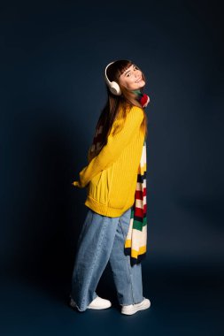 Güzel, genç bir kadın canlı, sıcak kıyafetler içinde neşeli bir gülümseme ve kulaklıkla poz veriyor..