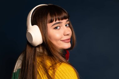 Kalın giyinmiş güzel bir kadın, karanlık bir arkaplanda aktif olarak poz verirken müzik dinlemekten hoşlanıyor..