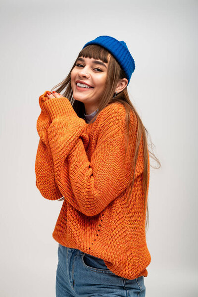 Молодая женщина в ярко-оранжевом свитере и голубой шапочке радостно улыбается, играя.