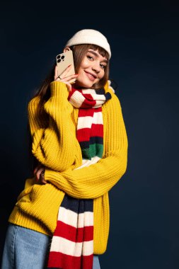 Genç bir kadın canlı kış pozu verirken ve telefonunu tutarken sıcak bir şekilde gülümsüyor..