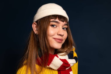 Kendine güvenen genç bir kadın şık kıyafetini koyu bir arka planda sergiliyor..