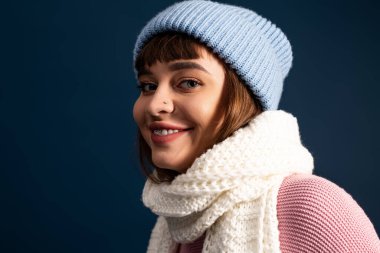 Güzel, genç bir kadın, koyu bir zemine karşı şık, sıcak kıyafetler içinde poz verir..