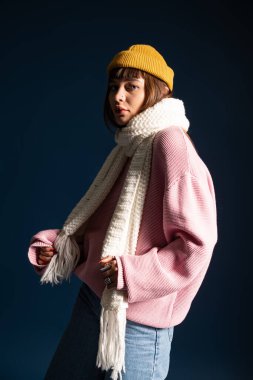 Ilık elbiseli canlı genç bir kadın koyu bir arka plana karşı poz veriyor, stil ve kendine güven yayıyor..