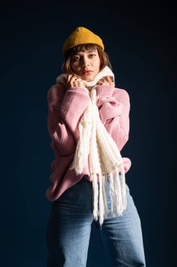 Genç bir kadın etkin bir şekilde poz verir, rahat bir şekilde giyinir, sonbahar ruhunun ortasında sıcaklığı yayar..