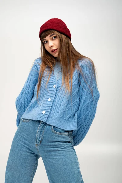 Serin bir günde, rahat mavi bir kazak ve kırmızı bir bereyle poz veren genç bir kadın..