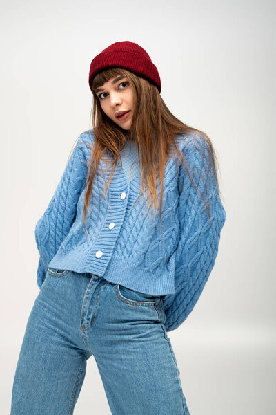 Молодая женщина позирует в уютном голубом свитере и красной шапочке в холодный день.