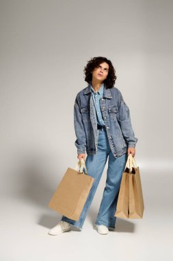 Confident woman in denim, stunning curls, joyfully holding shopping bags.