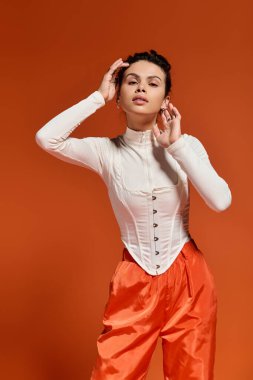 A stylish young woman poses confidently in a vibrant outfit in a studio.