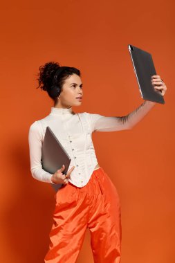 Beautiful young woman uses a tablet and laptop while showcasing her trendy style in vibrant colors.