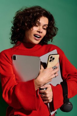 A young woman in a vibrant outfit joyfully embraces her tech gadgets against a bold backdrop.