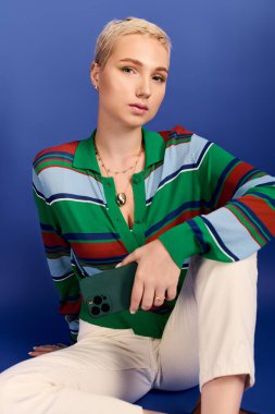 Şık, genç bir kadın canlı mavi bir arka planda kendine güvenerek kıyafetini sergiliyor..