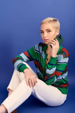 Tarz sahibi genç bir kadın akıllı telefonuyla yerde güven içinde oturuyor ve bakışlarını gösteriyor..