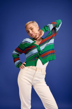 Güzel bir genç kadın, arka planı aydınlatan modaya uygun bir kıyafet sergileyerek kendine güvenerek poz veriyor..