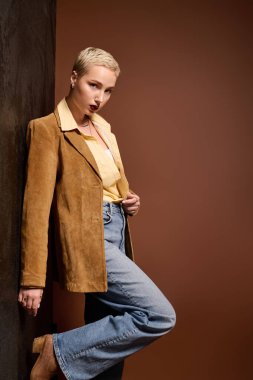 Genç ve güzel bir kadın, modaya uygun bir kıyafetle, duvara yaslanarak eşsiz tarzını sergiliyor..