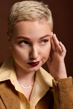 Kısa saçlı genç bir kadın şık tarzını kahverengi bir ortamda sergiliyor..