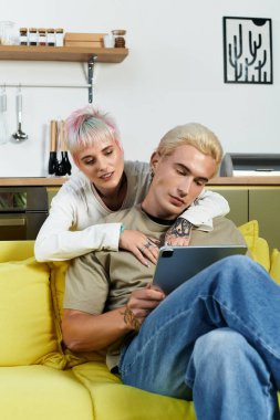 Sevgi dolu ortaklar koltukta sıcak ve samimi bir an paylaşırlar, cihazlarıyla meşgul olurlar..