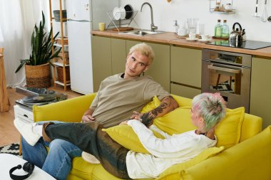 Çift sarı bir kanepede oturur, rahat ve canlı bir yerde birbirlerine eşlik ederler..