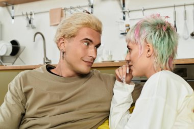 Genç bir adam ve kadın şık mutfaklarında dinlenirken birbirlerine sevgiyle bakıyorlar..