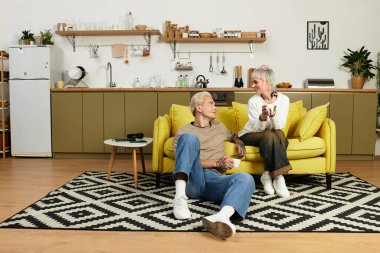 Çift, güzel düzenlenmiş oturma odasındaki sarı bir kanepede neşeli bir sohbet paylaşıyor..