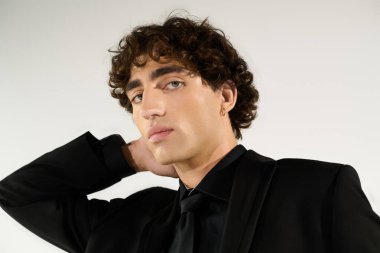 Genç ve yakışıklı bir adam kendine güvenerek poz veriyor, modaya uygun kıyafetlerini temiz bir arkaplanda sergiliyor..