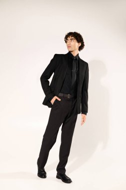 Yakışıklı genç bir adam şık siyah bir takım elbise içinde duruyor, kendine güveni ve tarzı var..