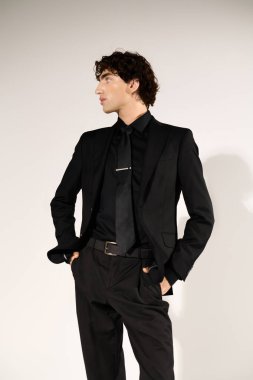 Yakışıklı genç bir adam şık siyah takımını sergilerken kendine güvenen bir duruş sergiliyor..