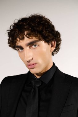 Adam şık giyiniyor ve basit bir arkaplana karşı modaya uygun siyah bir takım elbise giyiyor..