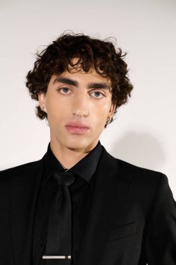 Yakışıklı genç bir adam şık bir siyah giysinin içinde kendine güvenerek duruyor. Havalı bir tarzı ve cazibesi var..