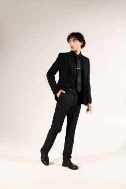 Siyah giyinmiş genç adam sade bir arka plana zarif bir şekilde poz veriyor..