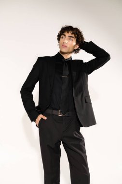 Gösterişli siyah elbiseli genç adam kendine güveni ve çekiciliğiyle duruyor. Tarzını vurguluyor..