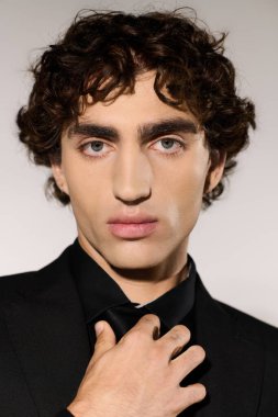 Şık giyinmiş, kendine güvenen genç bir adam basit bir arkaplana karşı zarif bir şekilde poz verir..