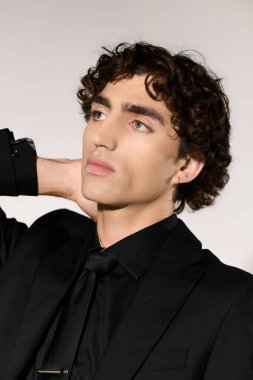 Kıvırcık saçlı genç yakışıklı adam şık siyah bir takım elbise ve kravat giyerken kendine güvenerek poz veriyor..