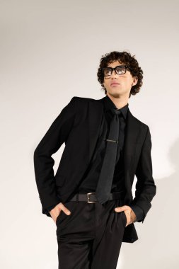 Gösterişli siyah takım elbiseli kendine güvenen genç adam şık bir poz veriyor..