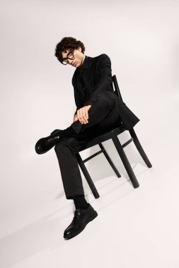 Zarif giyinmiş genç bir adam, modern moda ve tarzın somutlaştırılmış bir sandalyeye oturur..
