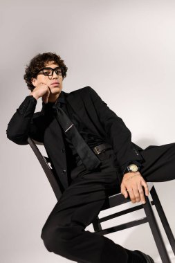 Şık siyah takım elbiseli ve gözlüklü yakışıklı bir genç kendine güvenen bir poz veriyor..