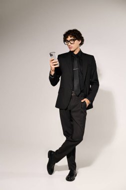 Parlak siyah takım elbiseli genç, yakışıklı bir adam telefonuna odaklanıyor, modern moda sergiliyor..