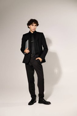 Şık giyinmiş genç ve yakışıklı bir adam stüdyoda dizüstü bilgisayarla rahatça poz veriyor..