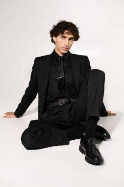 Yakışıklı adam kendine güvenerek oturur, şık siyah bir elbise içinde, modern moda anlayışı ve cazibesi yayar..