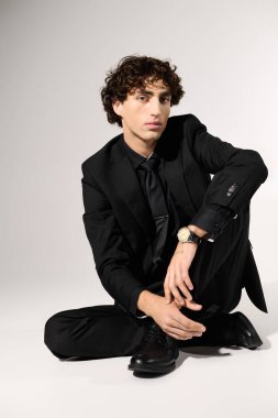 Siyah giysili şık genç adam, basit bir arka plana karşı güvenle poz verir..