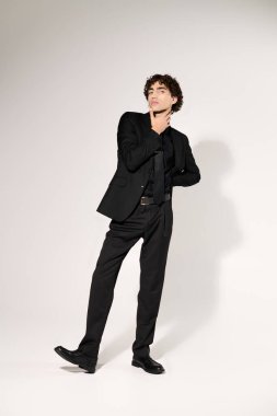 Yakışıklı genç adam moda anlayışını, şık siyah kıyafetlerini ve stüdyo içinde kendine güvenen pozlarını sergiliyor..