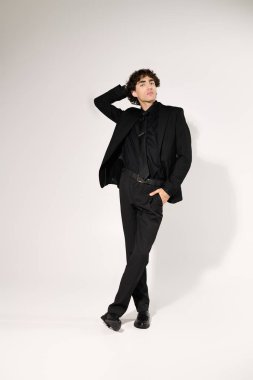 Kendine güvenen genç adam şık siyah bir takım elbise içinde şık bir duruşla duruyor..