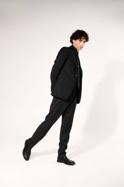 Genç yakışıklı adam şık siyah kıyafetleriyle moda anlayışını sergiliyor, kendine güveni tam..