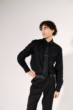 Pürüzsüz siyah elbiseli genç adam basit bir arka plana karşı özgüvenle poz veriyor..